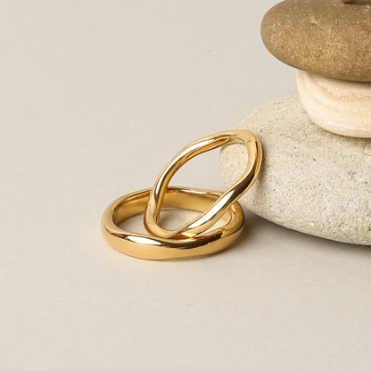 Gemini gold rings resting on pebbles
